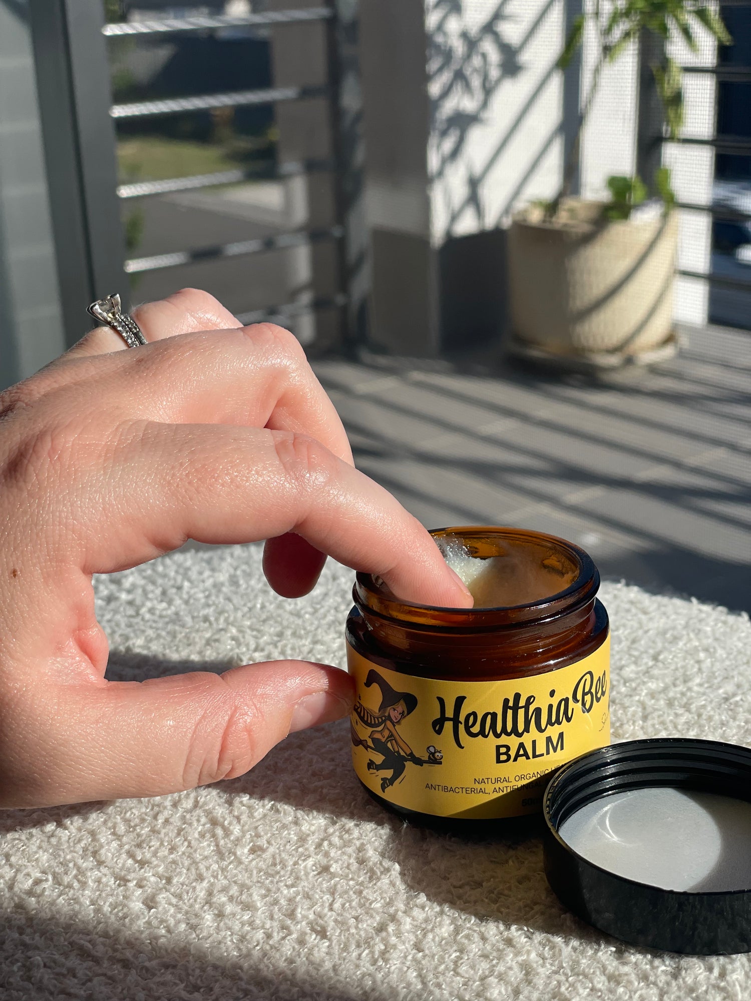 A person dips their finger into a jar of HealthiaBee Balm ready to apply it.