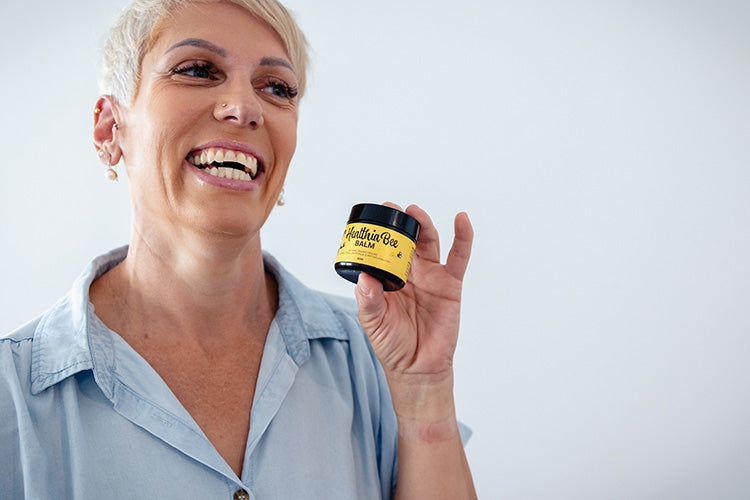 A lady smiles as she holds up a jar of Healthia Bee Balm