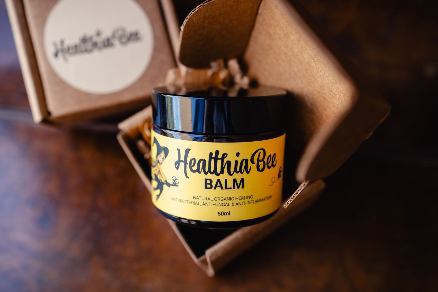 A jar of Healthia Bee Balm sitting in its eco-friendly cardboard box packaging. The label on the jar reads natural organic healing antibacterial, anti-fungal and anti-inflammatory.